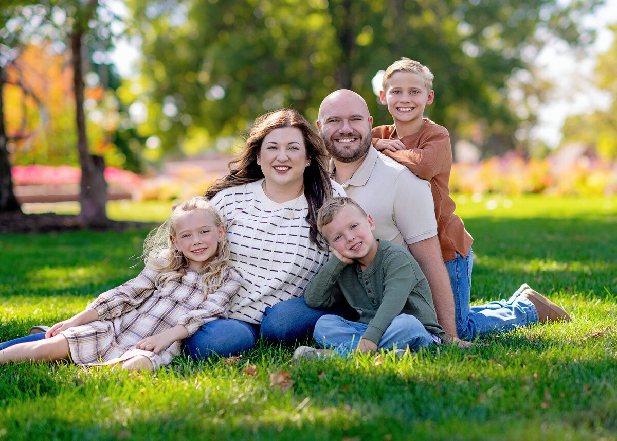 A family of 5 posing outdoors in a vibrant garden with greenery in the background