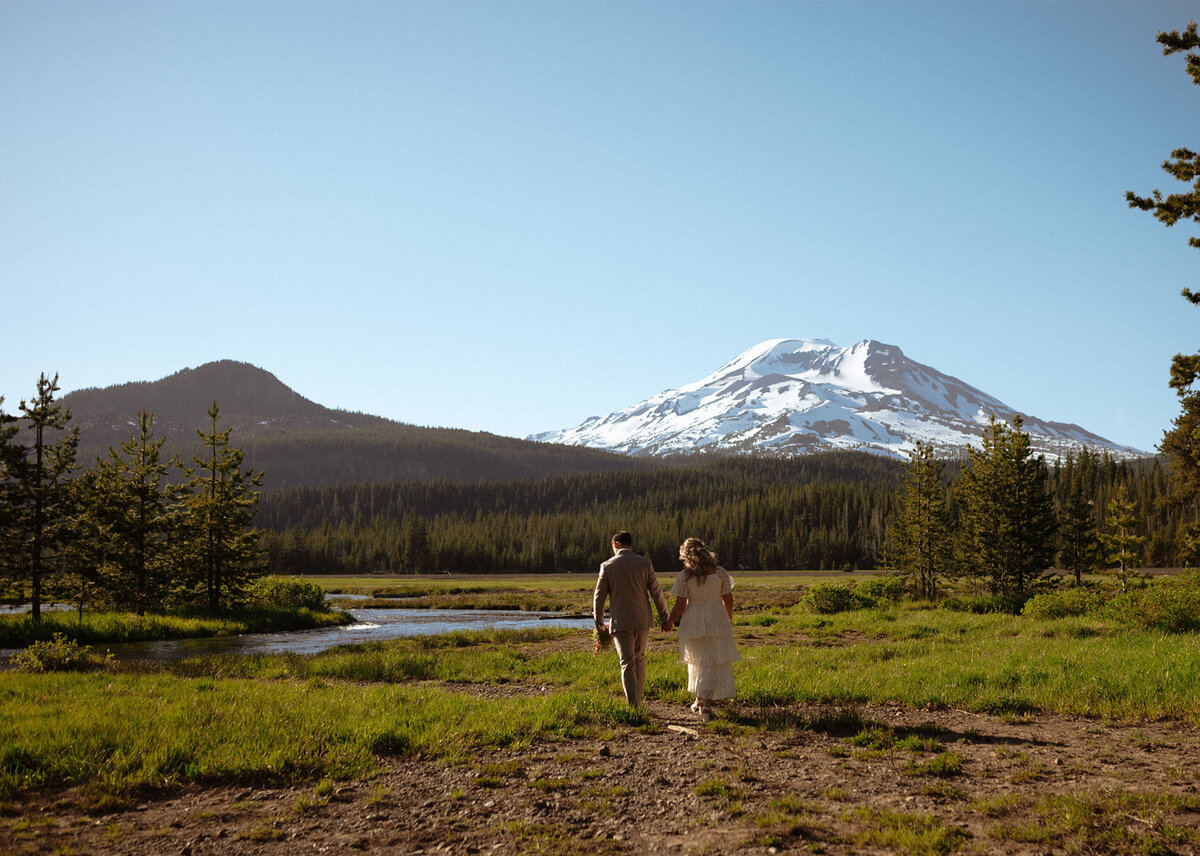 bride and groom walk along Sparks Lake on a sunny day with Mt. Bachelor in the background