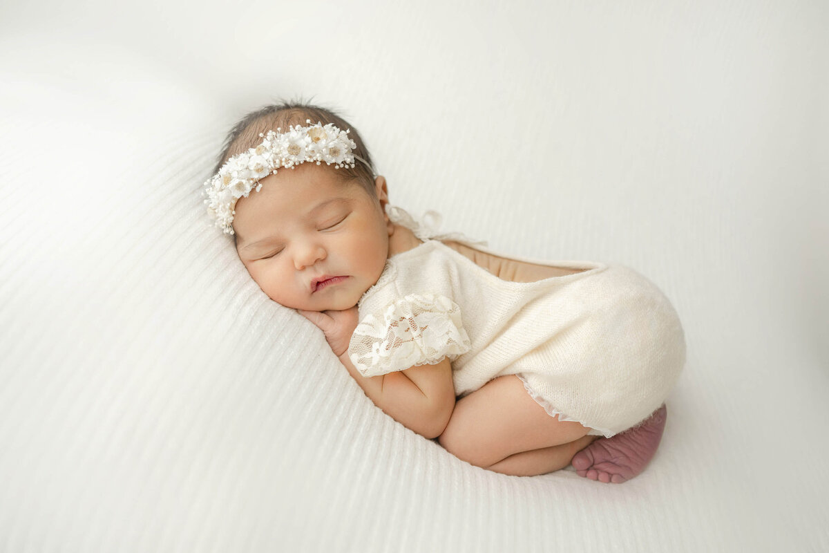 sleeping newborn on her belly wearing an adorable newborn onesie and floral crown
