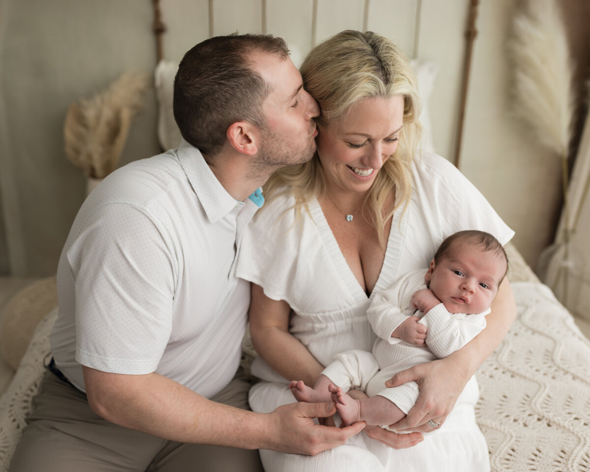 mom and dad holding newborn baby boy in white onesie for studio lifestyle session 