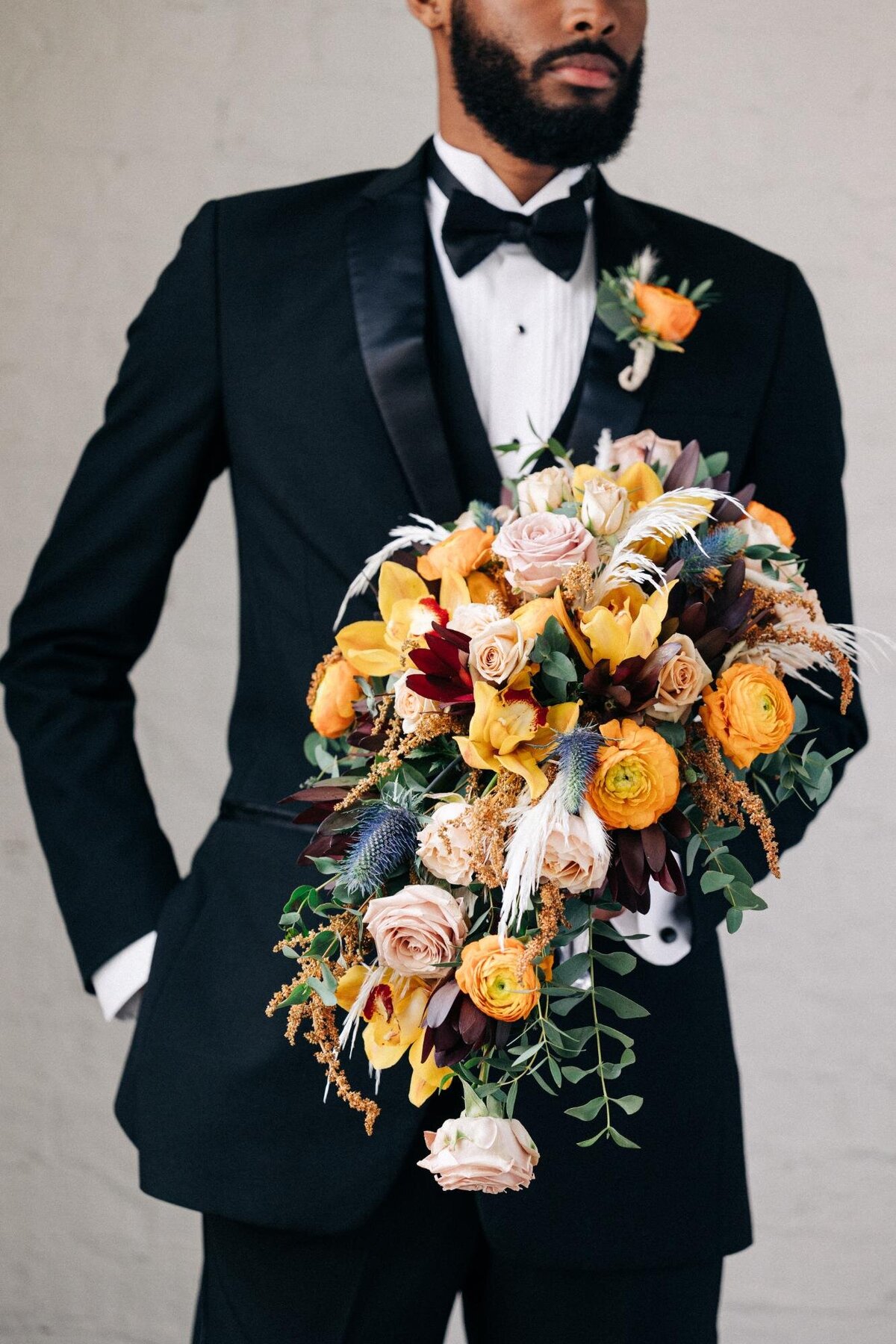 Man in a black suit holding a large floral bouquet.