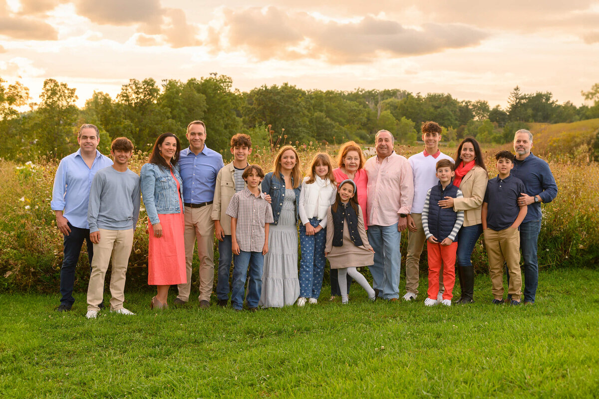 Extended Family photos of 16 people wearing coral and blue with the golden sun setting behind them for their summer extended family photography session