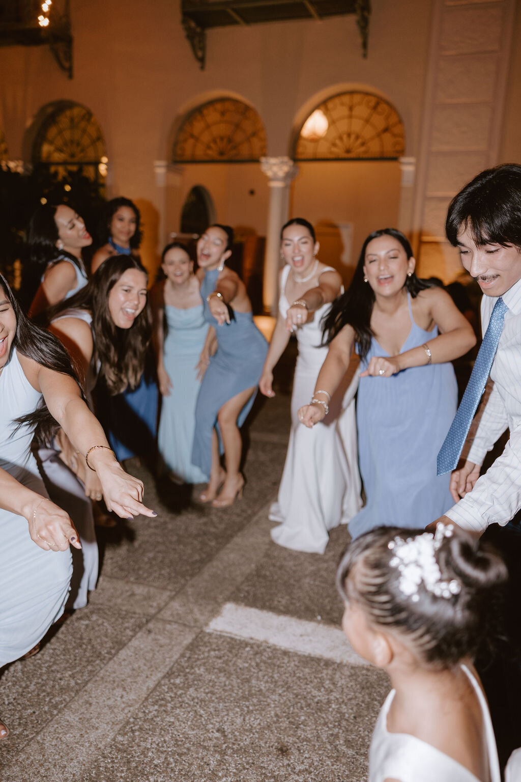 Women on dance floor of wedding reaching for a small girl coming forward excited and yelling