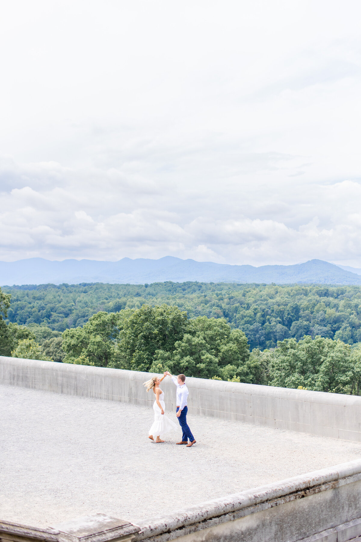 couple twirling around with scenic mountain view behind Biltmore Estate