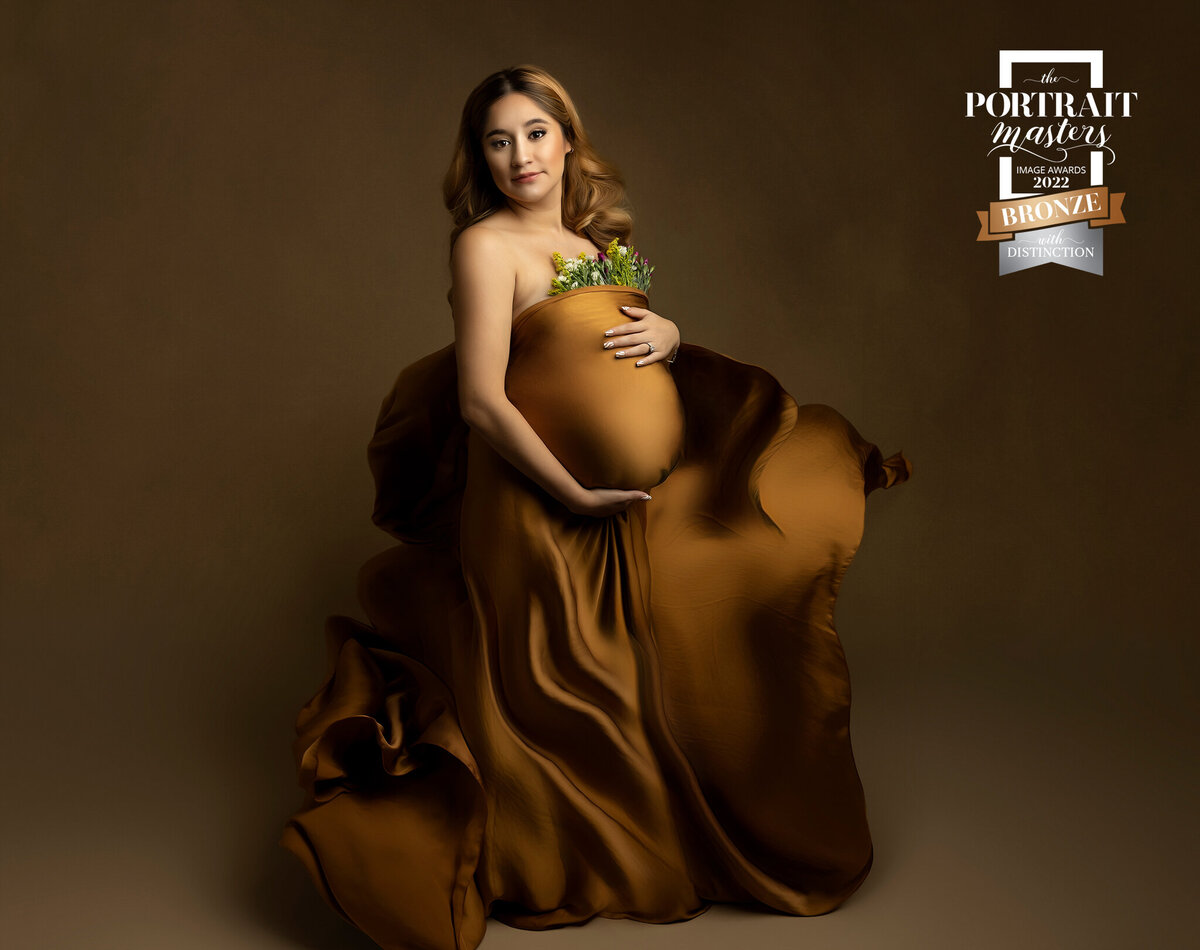 Maternity Photographer, woman  stands in studio in copper colored dress