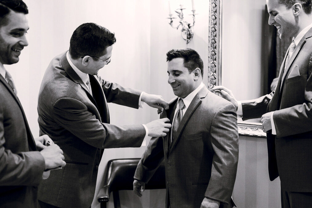 A group of groomsmen helping each other with their suits.