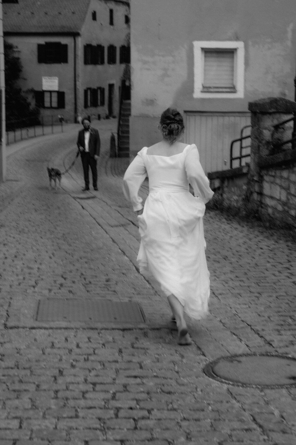 Der Bräutigam wartet im Hintergrund mit dem Hund, als die Braut auf ihn zu rennt.