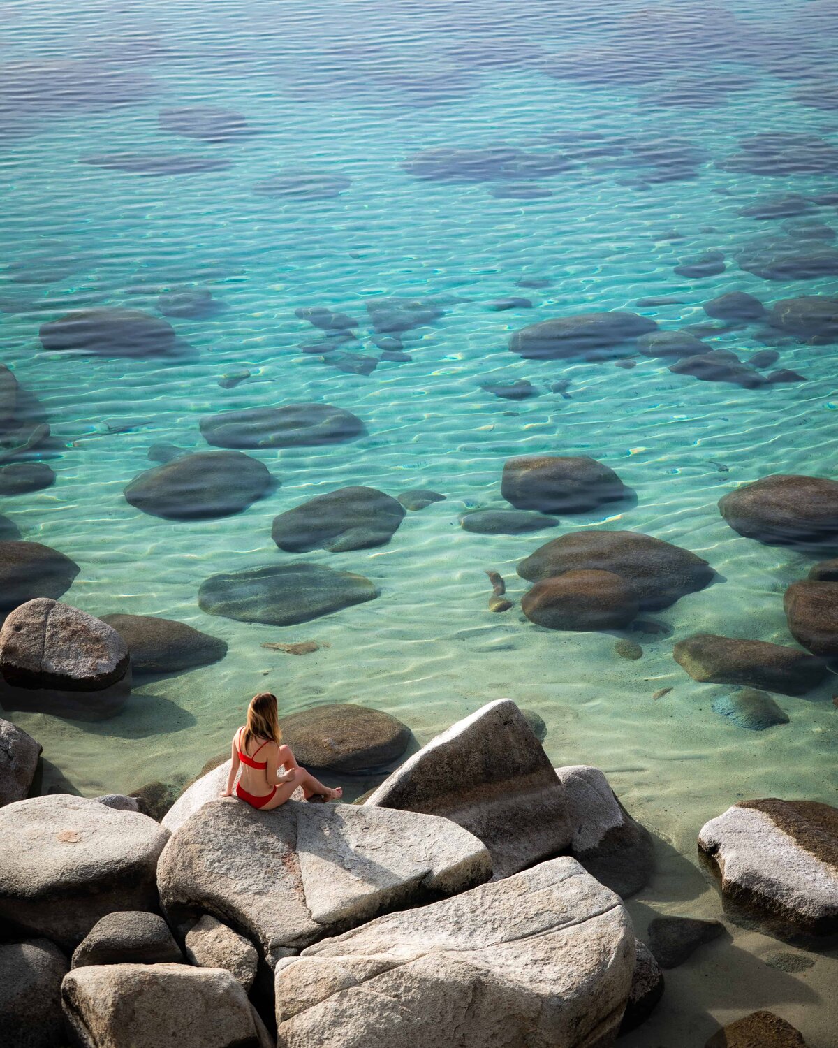 Woman in a red swimsuit sitting on a rock looking out at Lake Tahoe