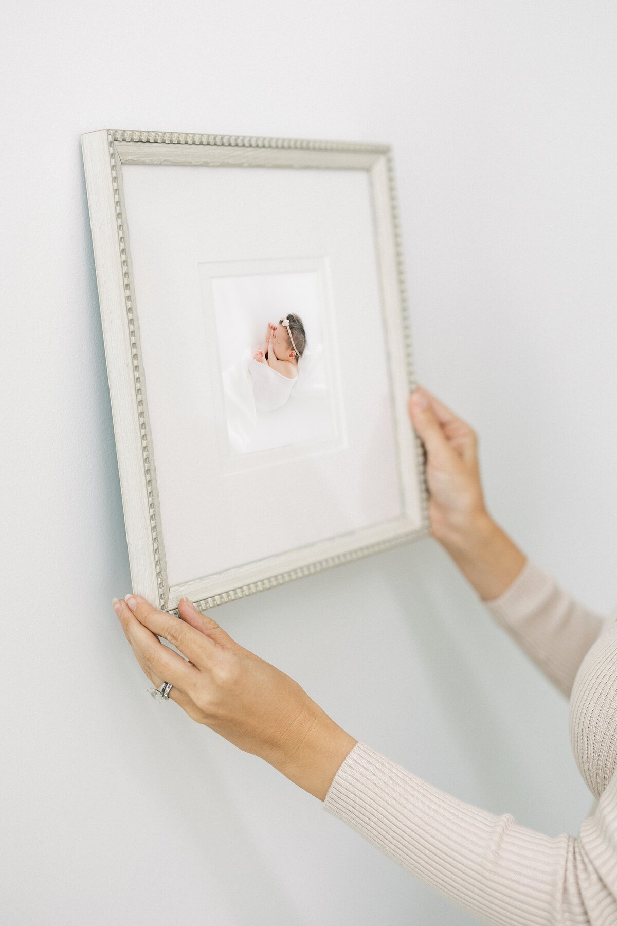 Framed portrait of newborn baby being hung on the wal by photographer Amanda Carter