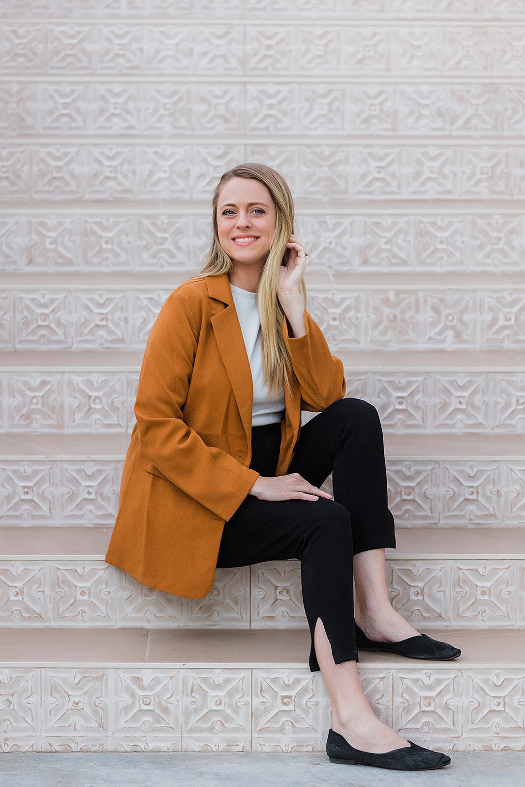 Headshot of a woman wearing a yellow blazer and black pants, sitting on stairs