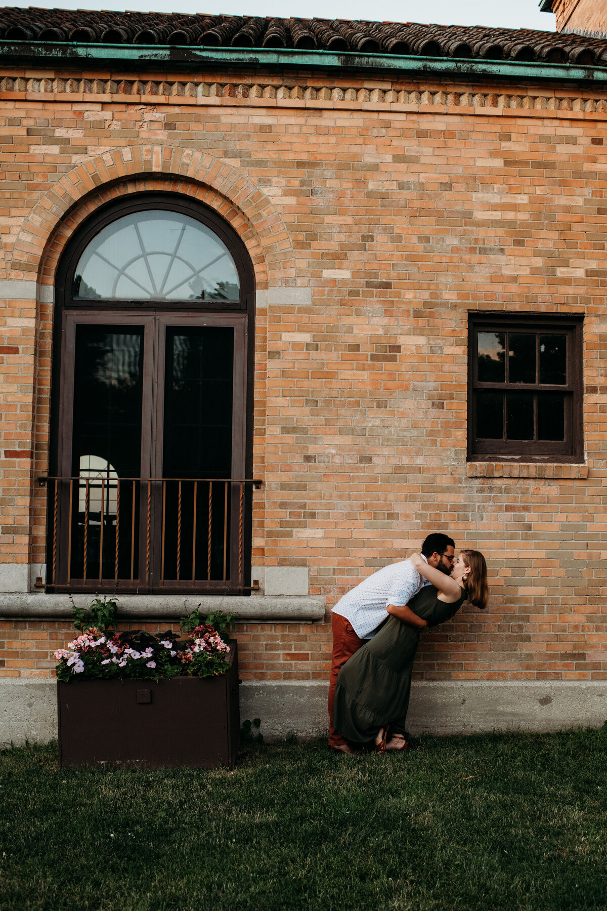 Man dipping woman and kissing her in front of brick building