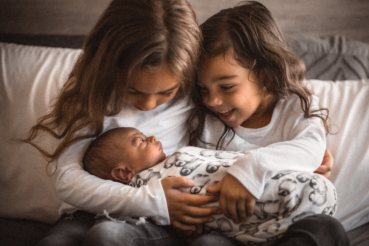 siblings smiling at newborn baby