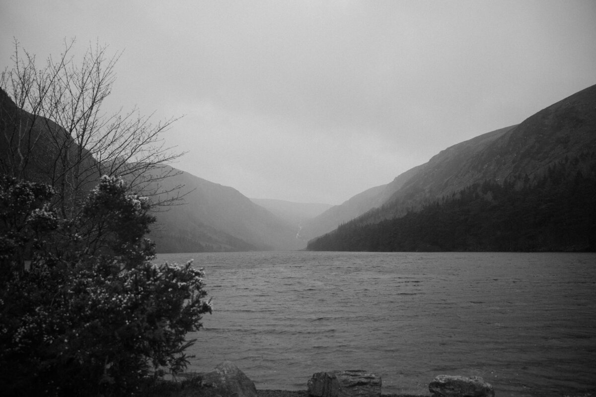 A monochrome landscape of Wicklow National Park with a serene lake nestled between foggy hills