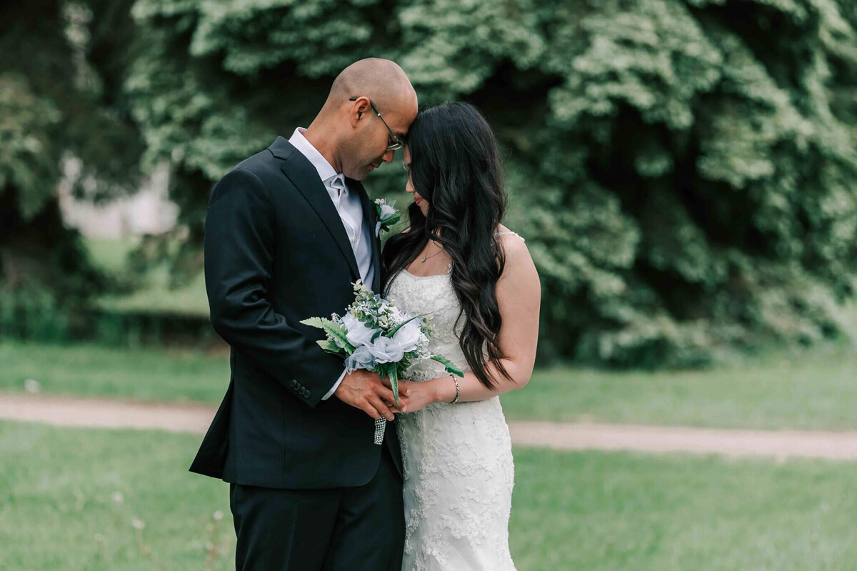 Bride and groom standing facing each other with their foreheads touching.
