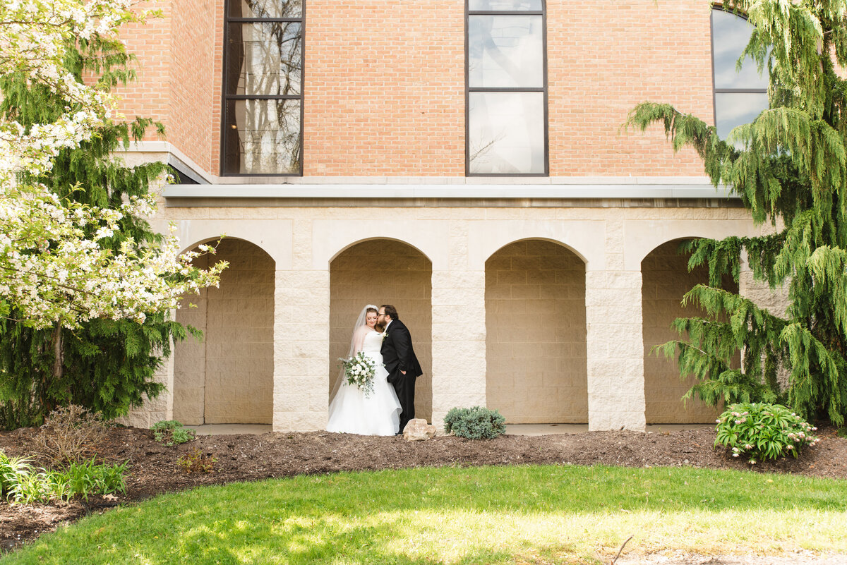 groom kisses brides cheek while they stand under archway outside of church