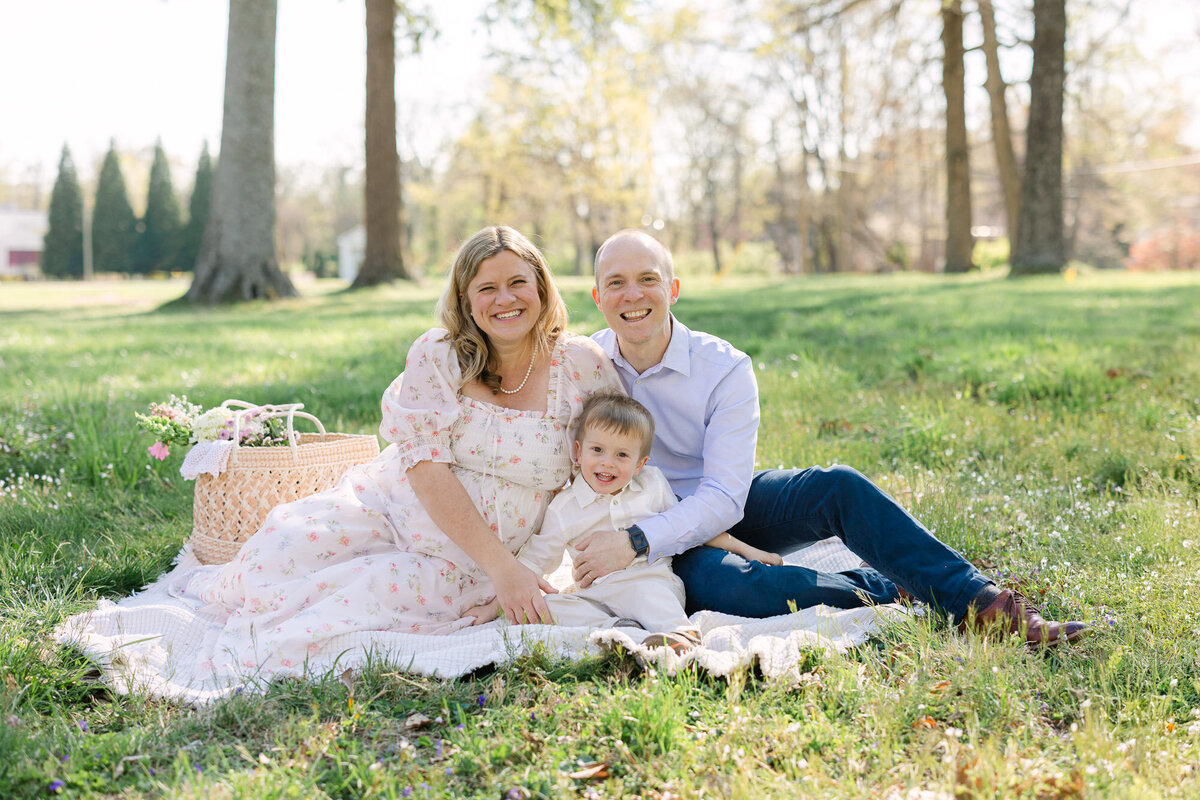 Portrait of an expecting mother wearing a light floral dress lying on a white blanket in a green field in Louisville kentucky
