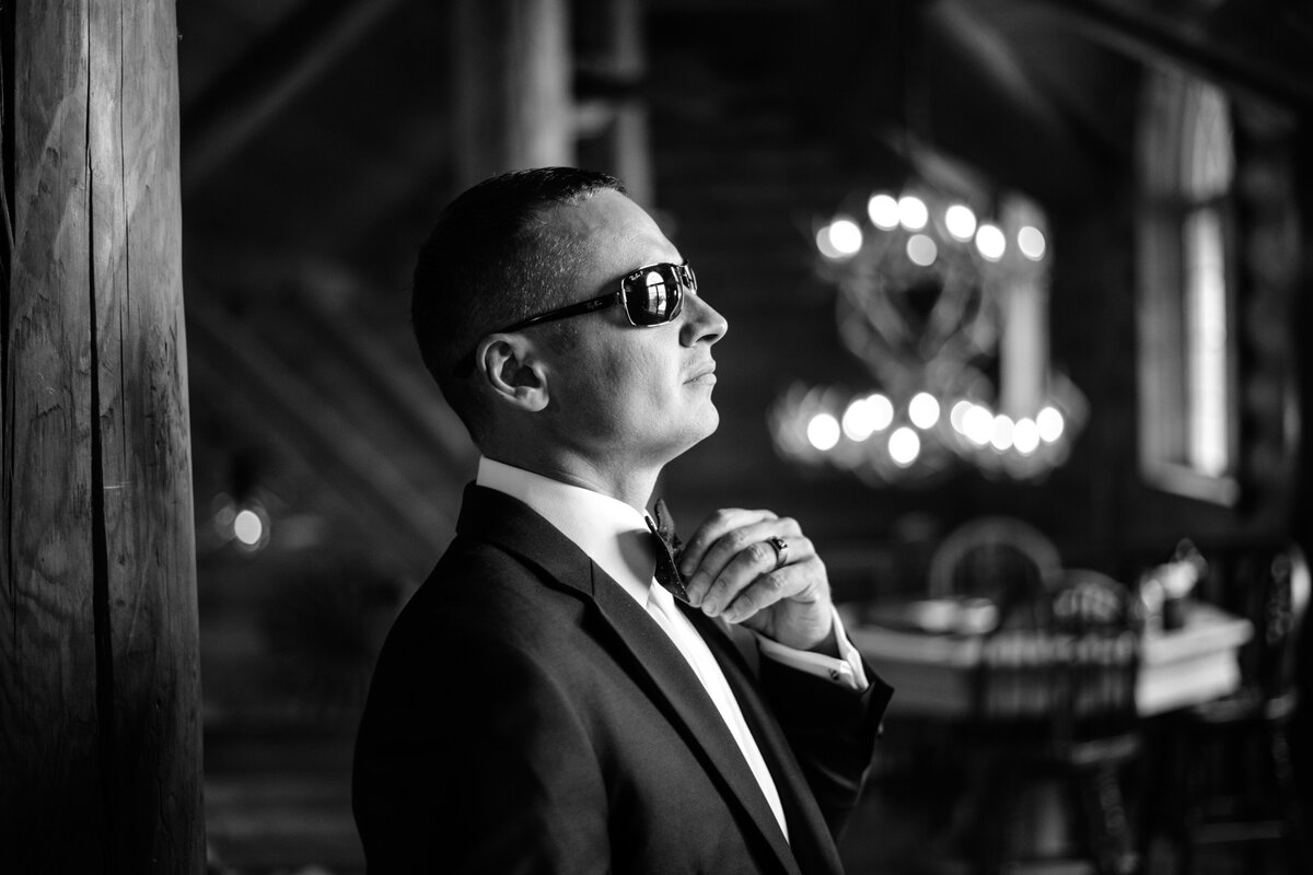 black and white picture of groom in sunglasses adjusting his tie