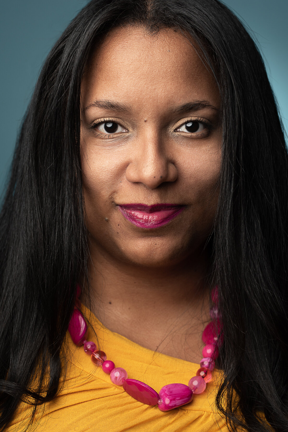 Headshot of a woman with a yellow shirt and pink necklace