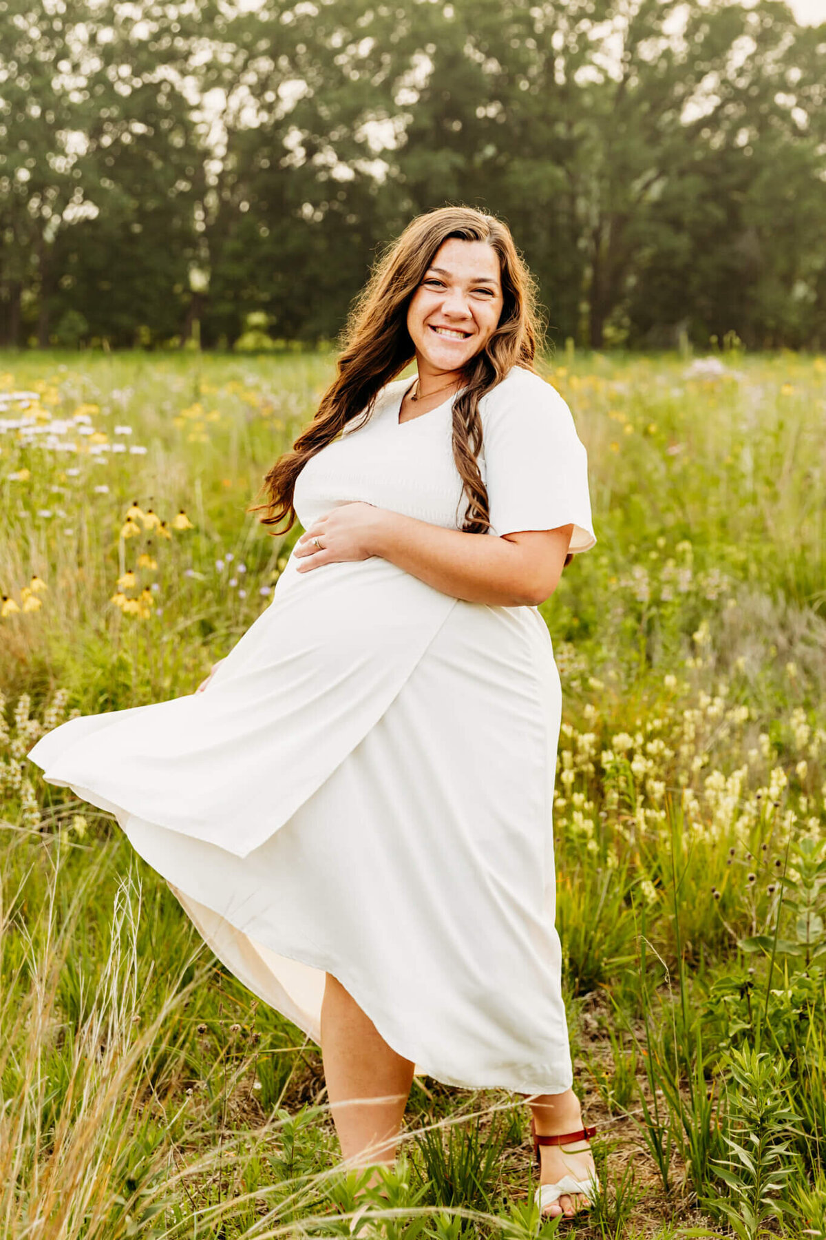 pretty pregnant mom playing with her white dress in a field of wildflowers near Green Bay