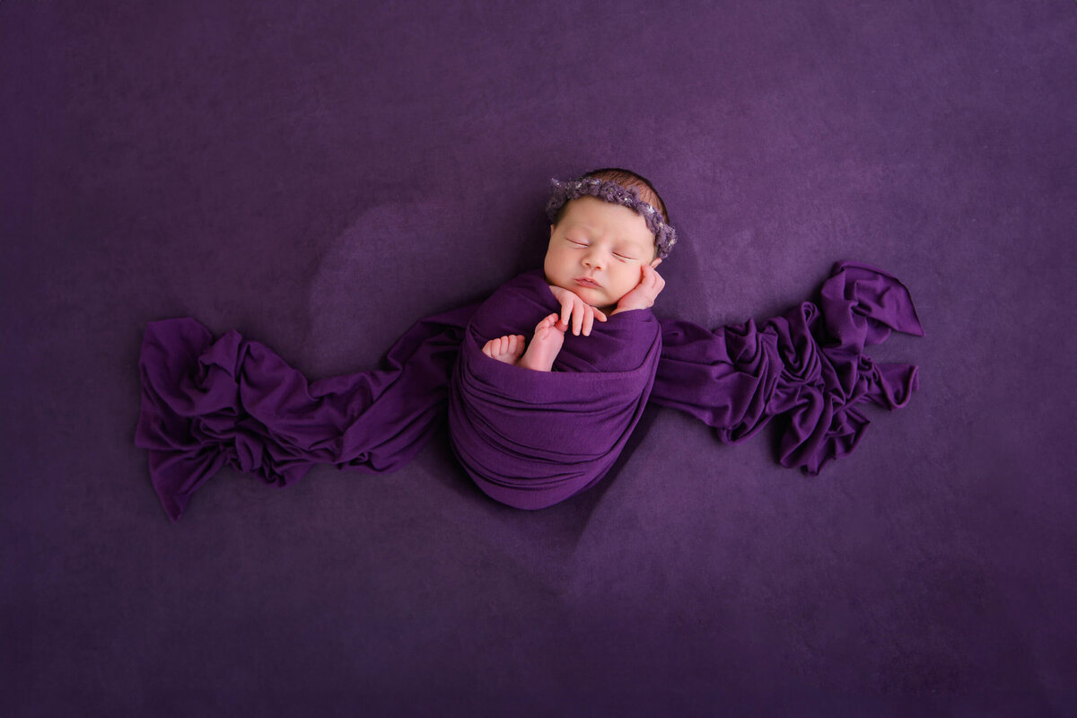 newborn baby girl wrapped in purple on a purple background in a heart bowl for her Burlington, ON newborn photography session
