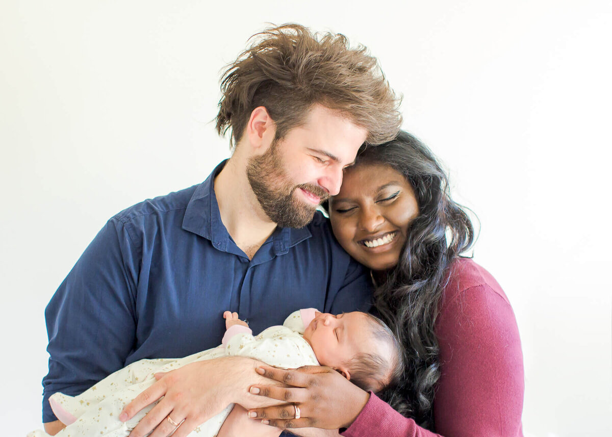 A interracial couple smiling and holding their baby