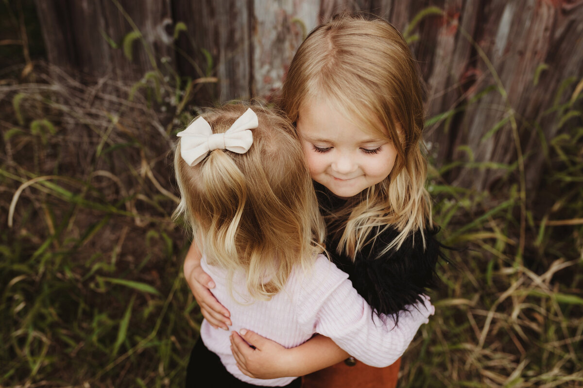 Two sisters are hugging each other sweetly.