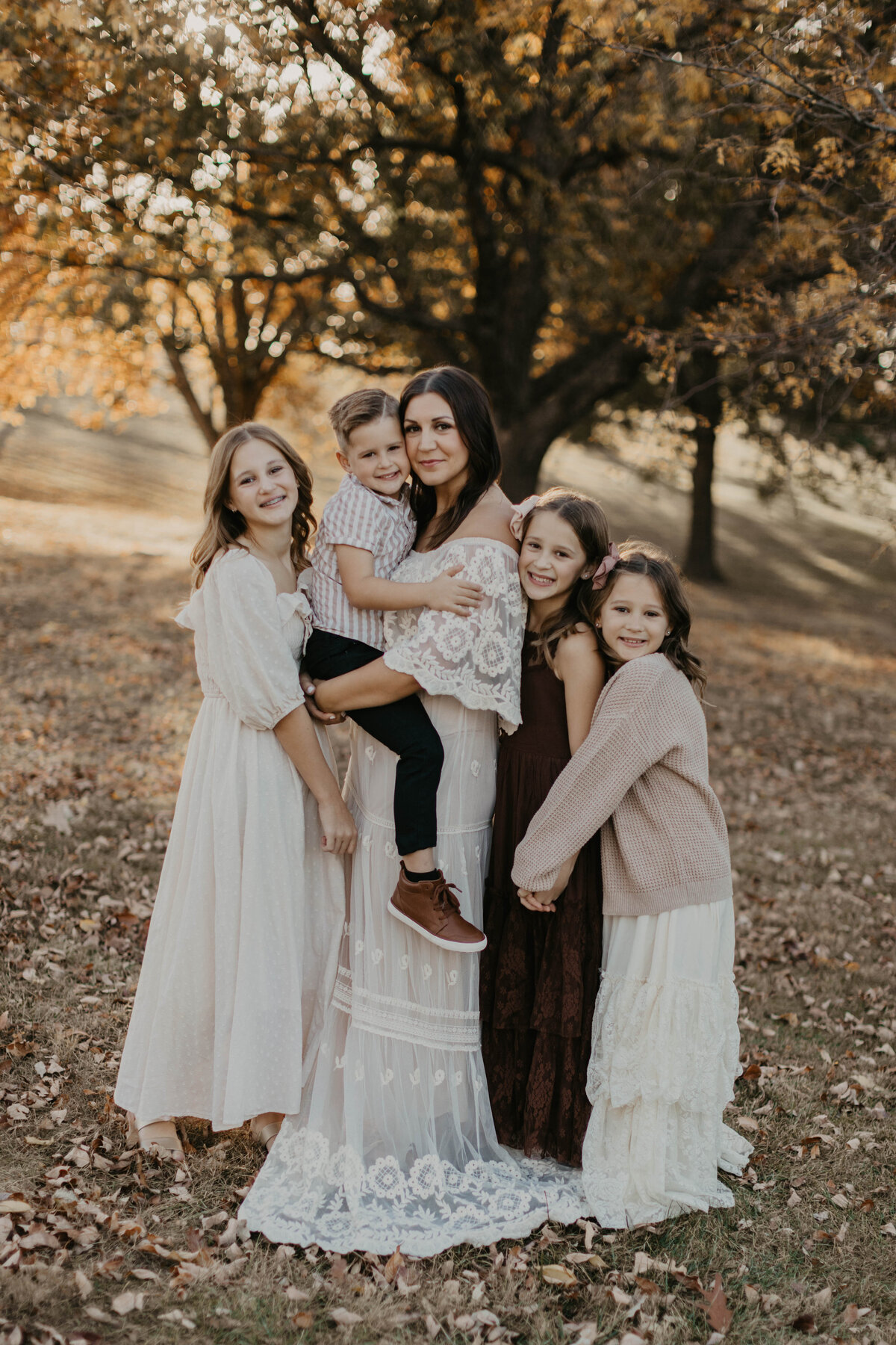 Mom holding her youngest child while the other three kids gather around her legs.