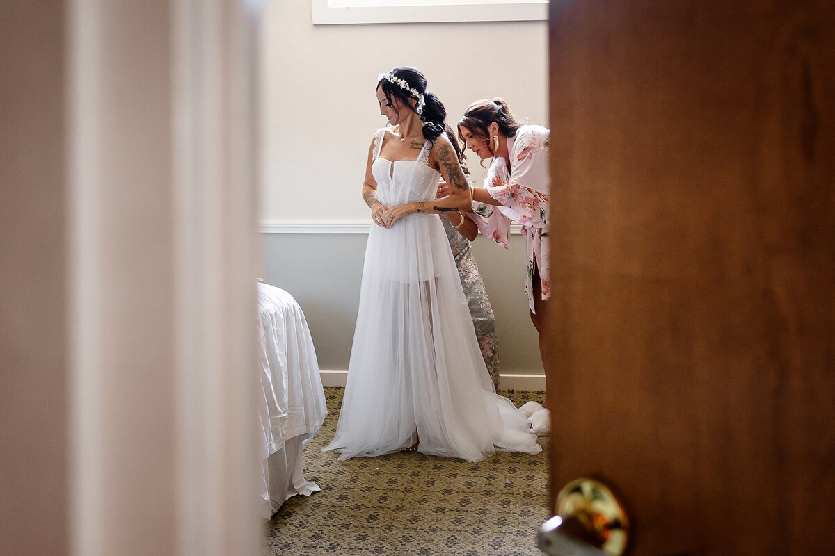 bridesmaid buttoning up brides gown in lakes region hotel.