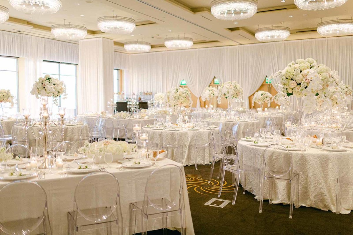 all white wedding reception with round and long tables, ghost chairs, and large white orchid centerpieces