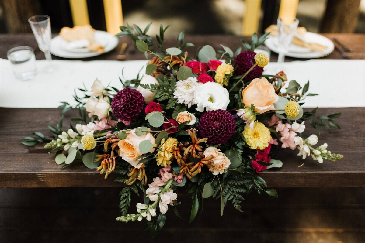 Large floral arrangement sits at the sweetheart table at a wedding.