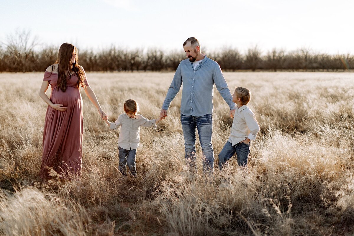 family of four with mama pregnant walking in the grass field
