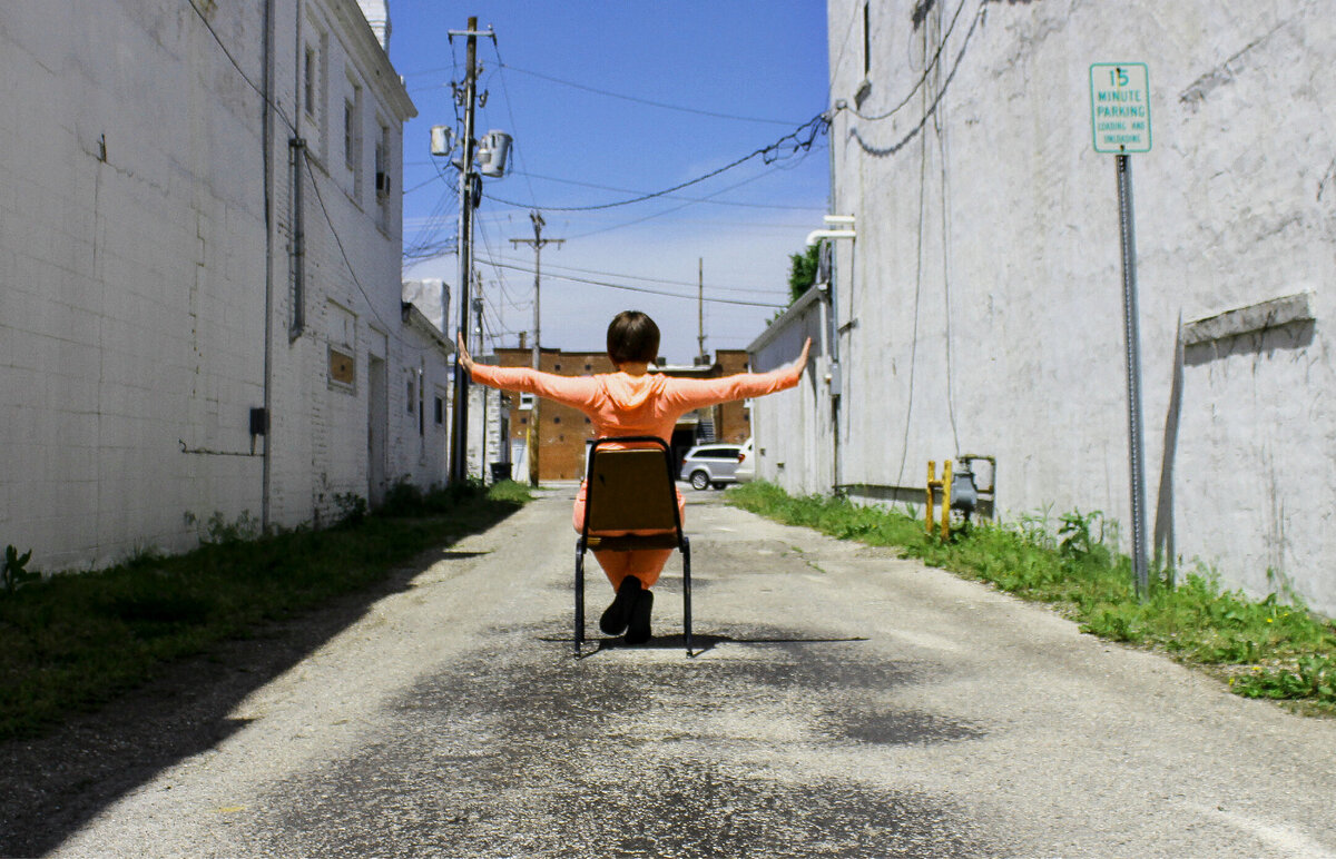 Image of Kelli standing in an alley with her hands in her hoodie pockets
