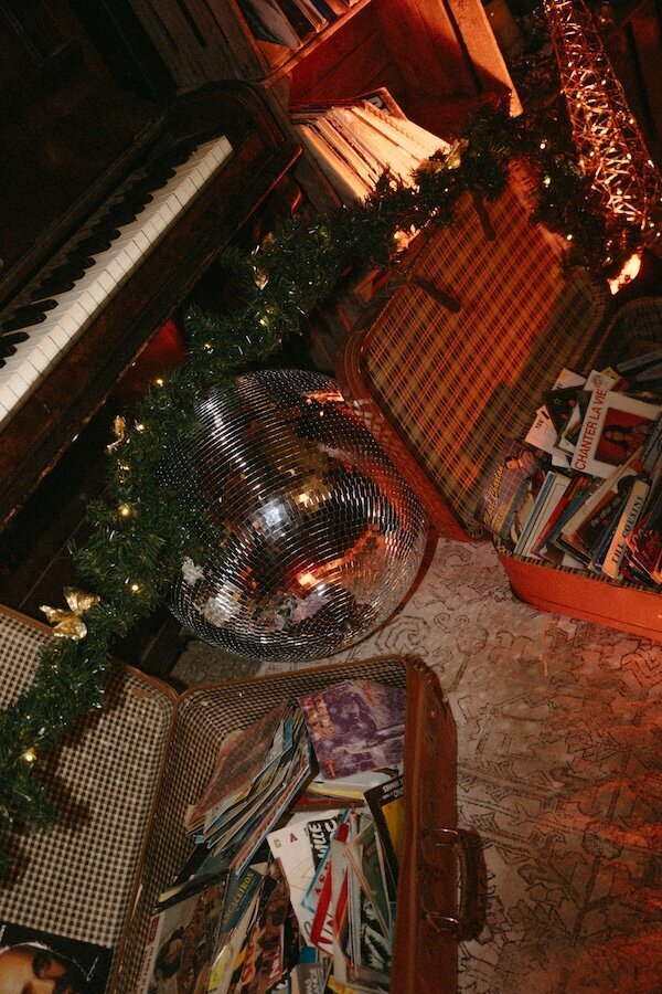 Coin cosy avec piano et valises remplies de vinyles, décoré de guirlandes et boule à facettes. Reportage de mariage authentique et vintage par Kamescop.
