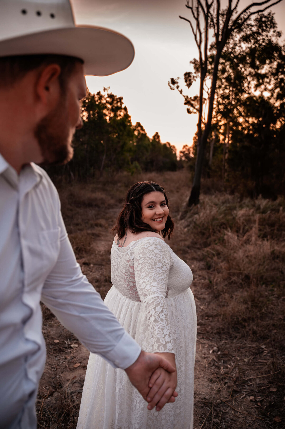 pregnant woman in white gown leading partner into the horizon along country road - Townsville Maternity Photography by Jamie Simmons
