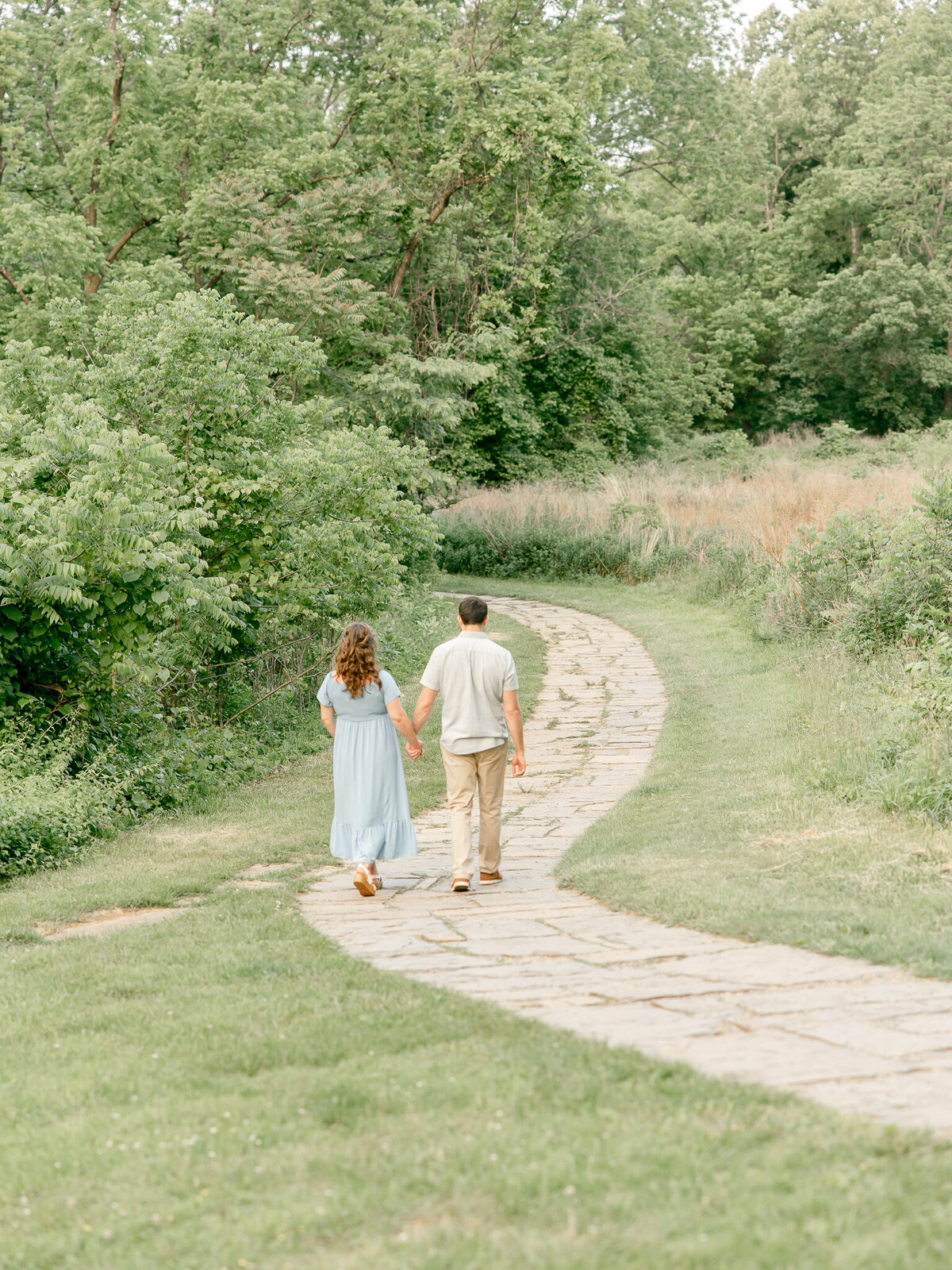 a couple walking away from the camera down a walking path at a park