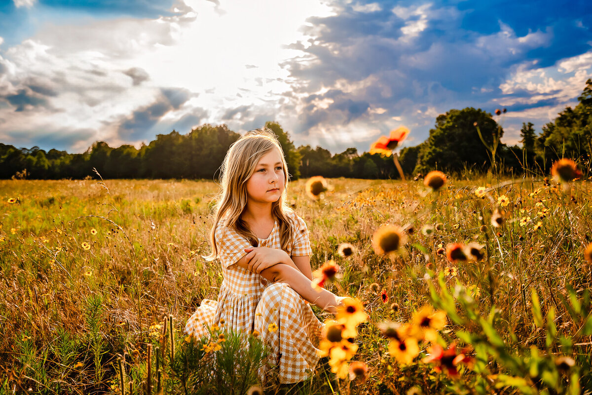 Young girl in a field of wild flowers under blue skies at sunset during spring