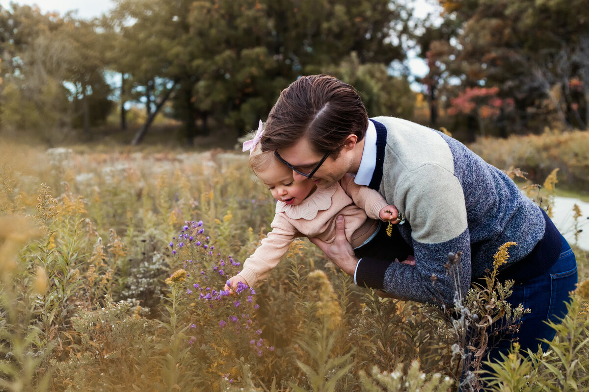 Father and daughter picking wildflowers during golden hour.