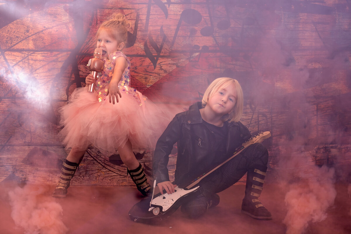 Edgy fine art portrait of two children dressed as rockstars, surrounded by vibrant lighting effects. Captured in Overland Park, Kansas, this bold and creative setup is perfect for families seeking unique and artistic child photography.