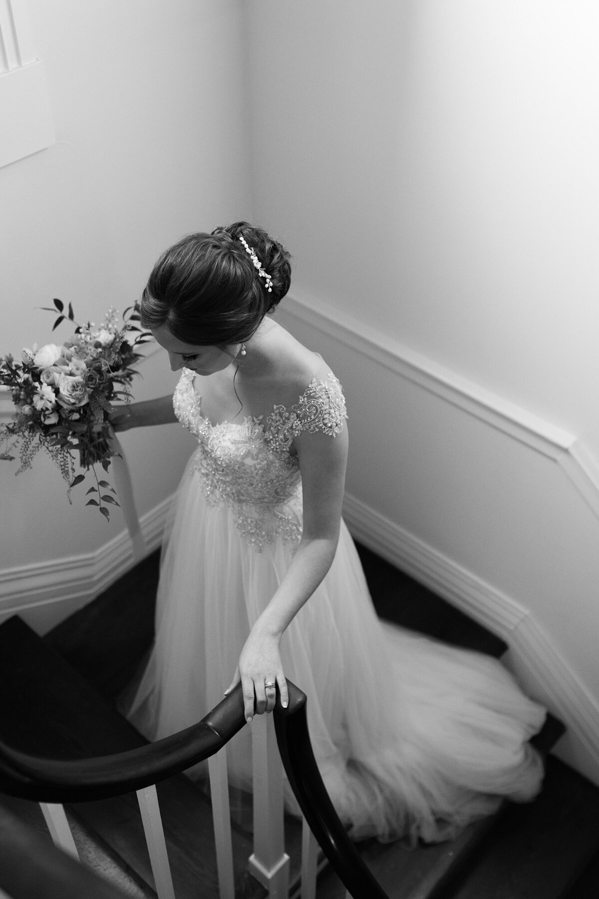A black and white photo of a bride going up a historic staircase at her venue in Charlotte, NC.