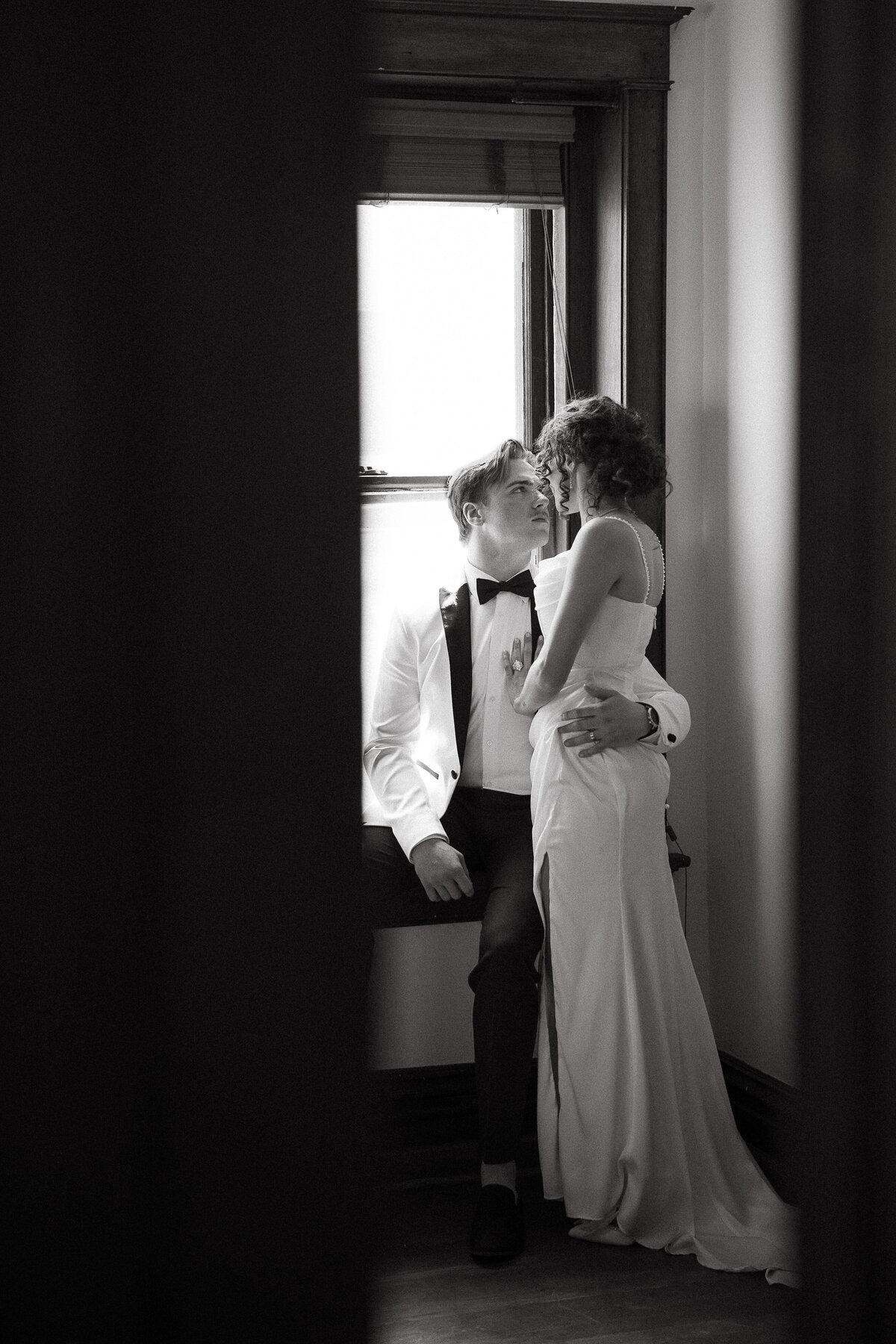 A bride and groom enjoy and intimate and quiet moment hugging. Photograph taken through a cracked doorway