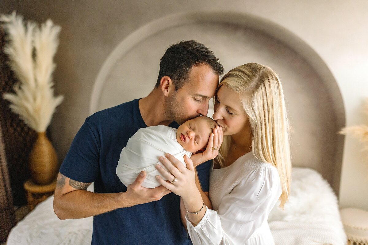 Mom and dad kissing newborn baby boy