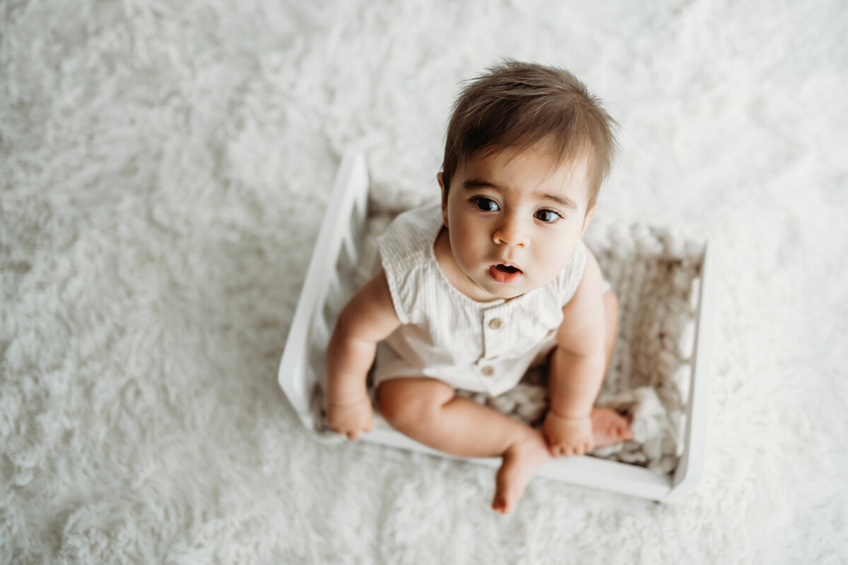 Six month old baby boy sitting on a small wooden bed for a milestone photo session in Denver. 