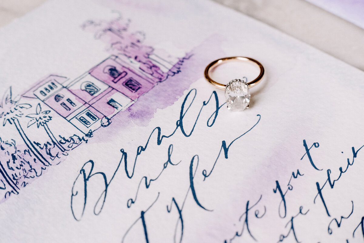 Gold ring with diamond in the middle, placed on top of the wedding invitation