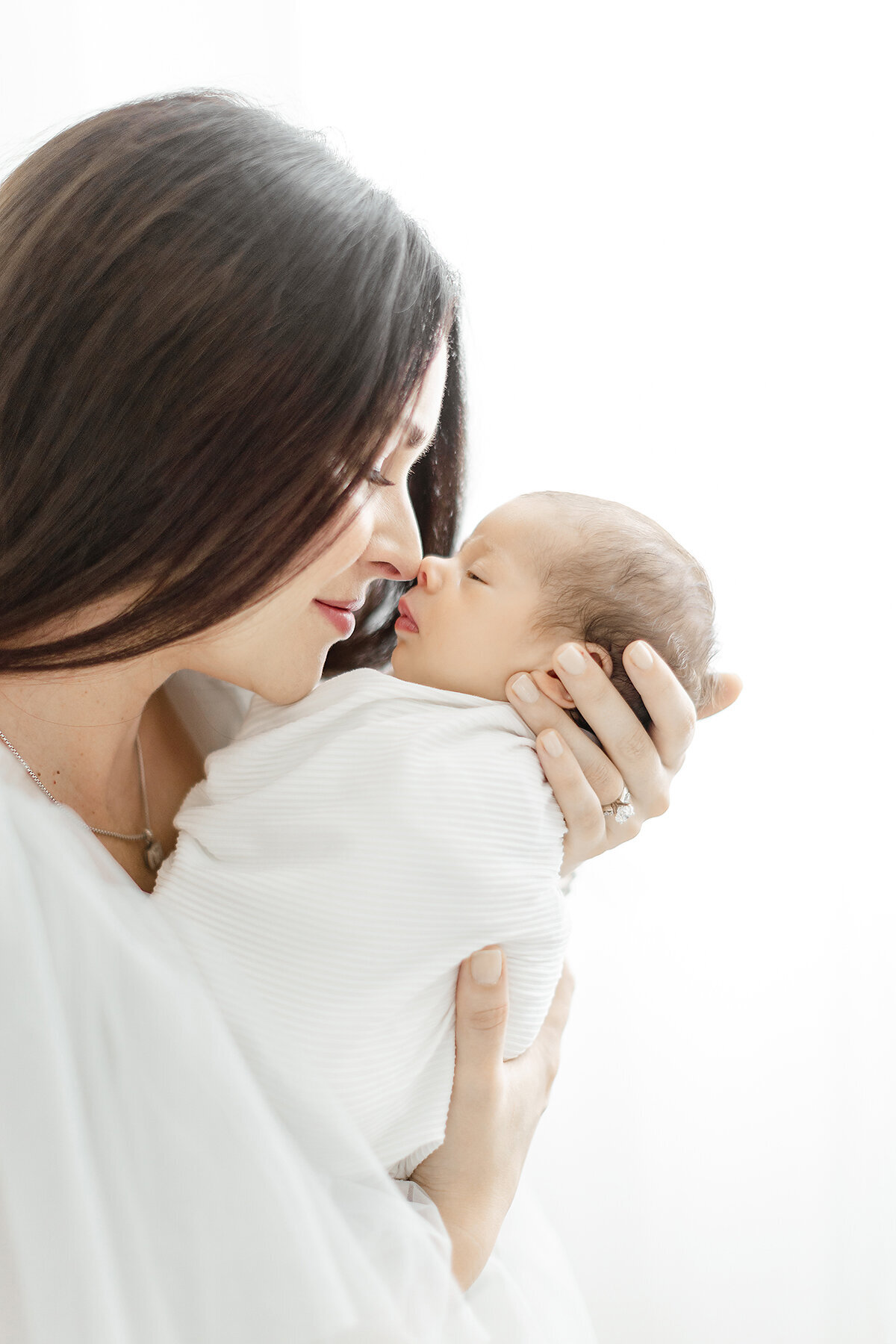 Close up photo taken as a side profile of a mother standing in a Dallas photography studio holding her newborn baby boy up as they touch noses.