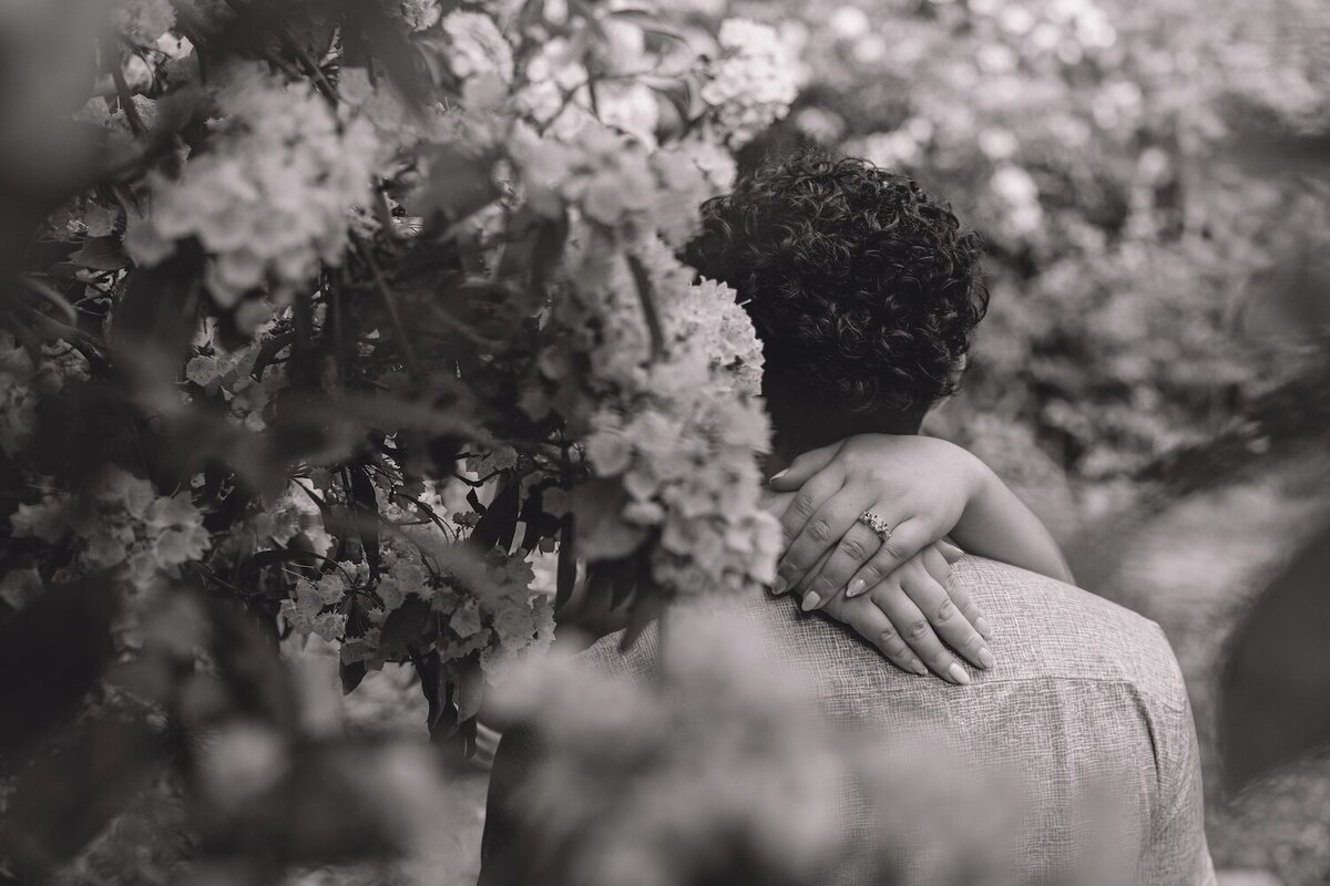 Black-and-white photo of couple kissing among blooming flowers.
