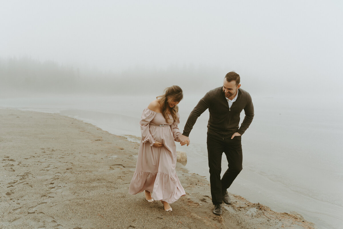 maternity photo of a couple  walking across a foggy beach