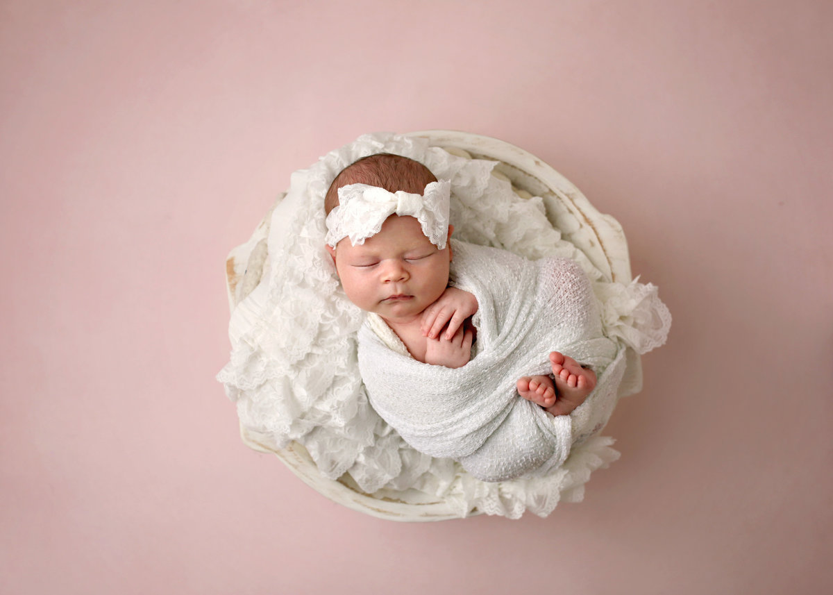 newborn baby girl wrapped in white posed in white basket
