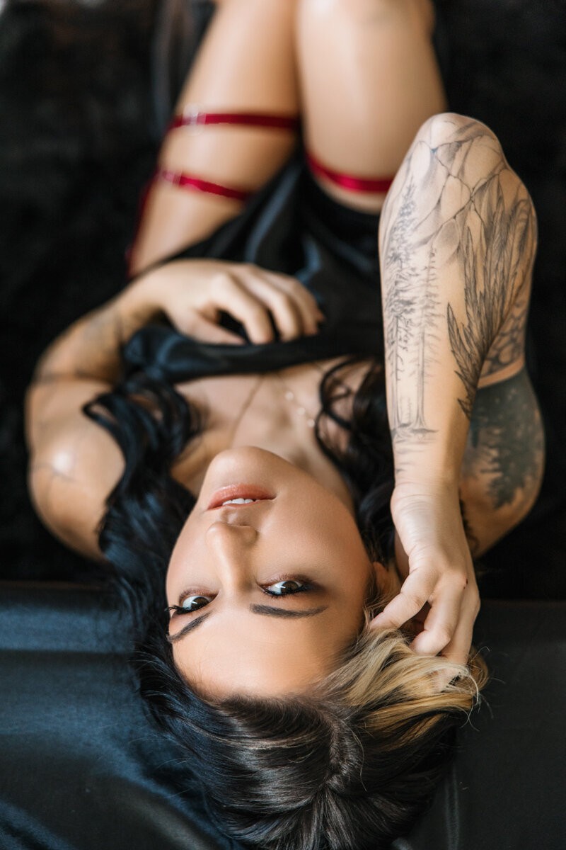 woman with tattoos wrapped in black satin sheets