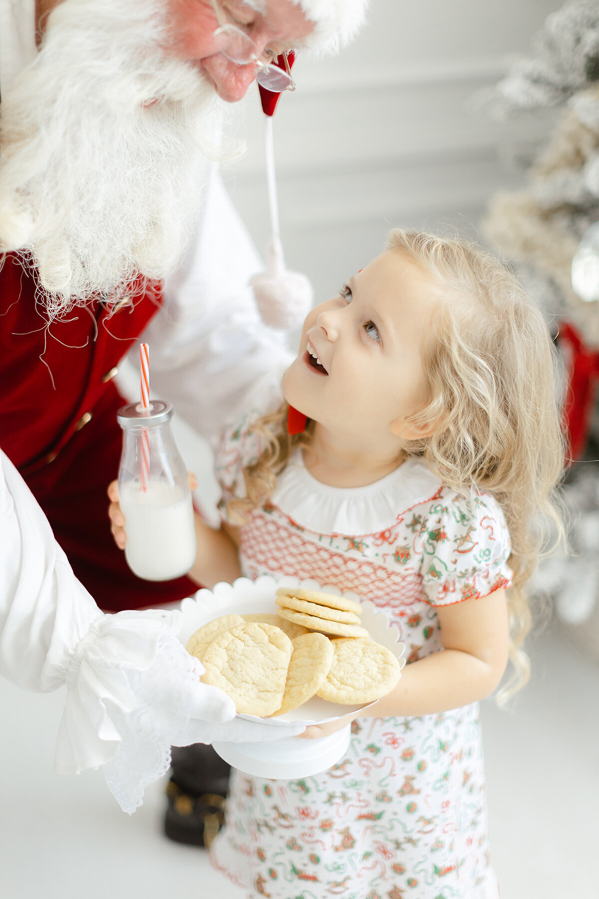 Close up photo of a little girl wearing a Dondolo christmas dress while santa hands her a plate of cookies.