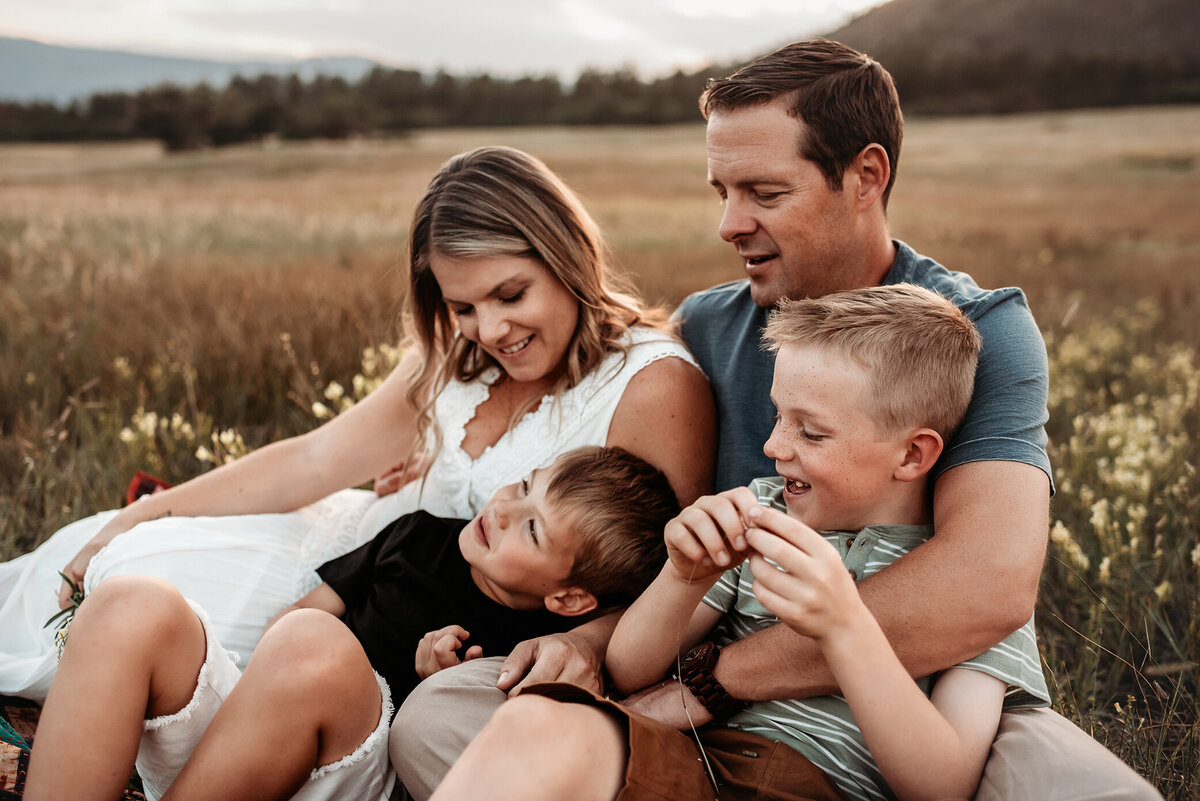 denver family photography of parents with two sons snuggling together in the summer grass